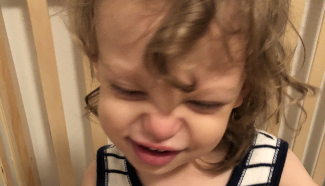 A toddler with curly hair scrunches their face and cries, wearing a blue and white striped shirt.