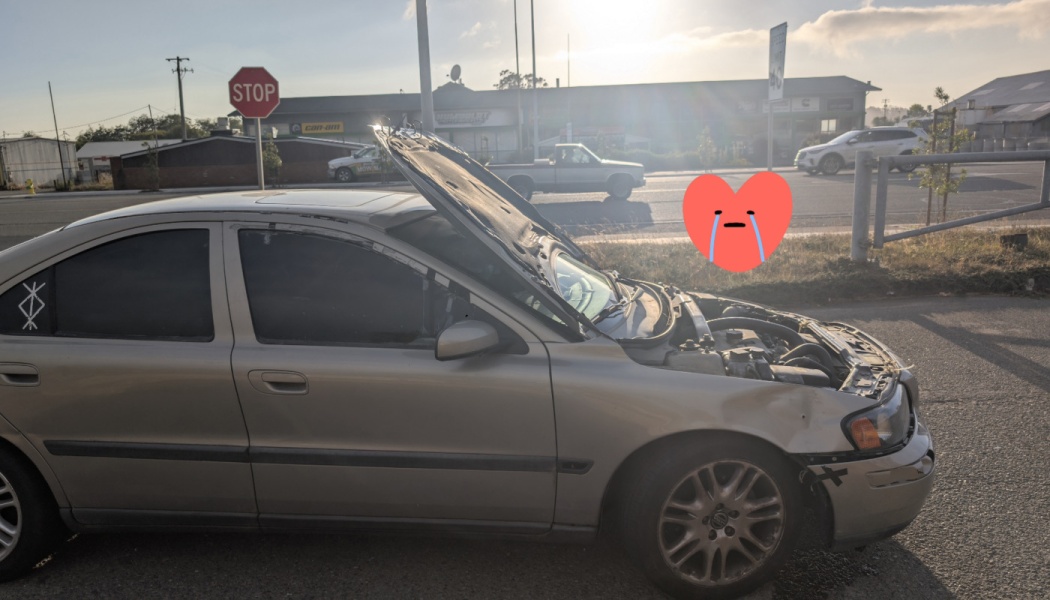 A damaged silver sedan with a buckled hood flipped wide open after a front-end crash.