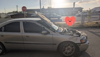 A damaged silver sedan with a buckled hood flipped wide open after a front-end crash.