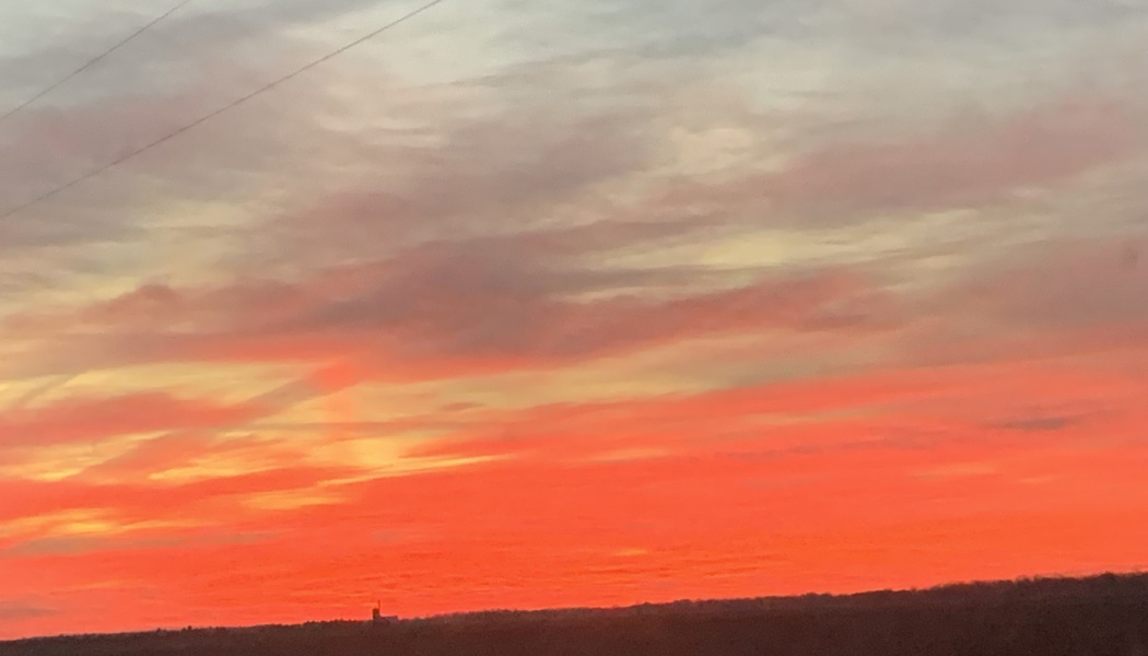 Vibrant fiery red and orange sunset filling a cloudy sky above a dark horizon.