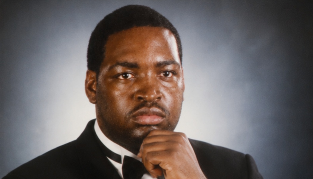 Formal portrait of a Black man in a tuxedo resting his chin on his hand with a thoughtful expression.