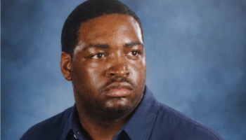 Headshot of a Black man with a serious expression, wearing a dark blue shirt against a blue backdrop.