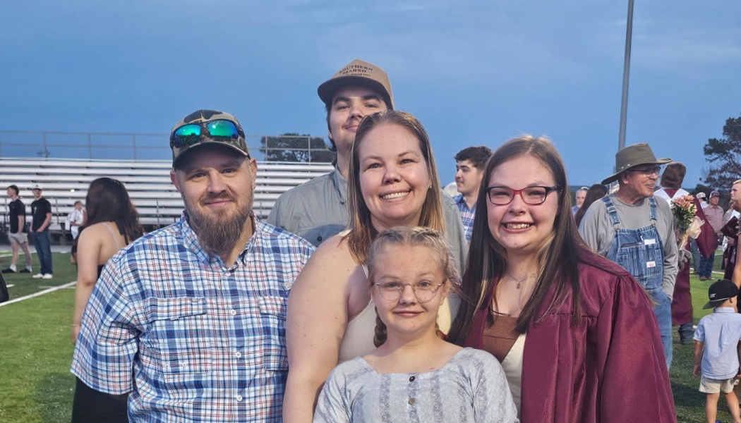 A smiling family of five posing on a football field to celebrate a high school graduation.