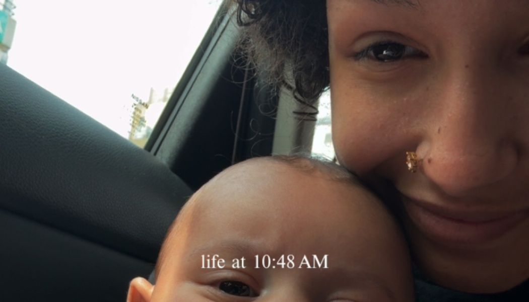 A smiling woman with a nose piercing posing close to her baby in a car, with text reading "life at 10:48 AM".