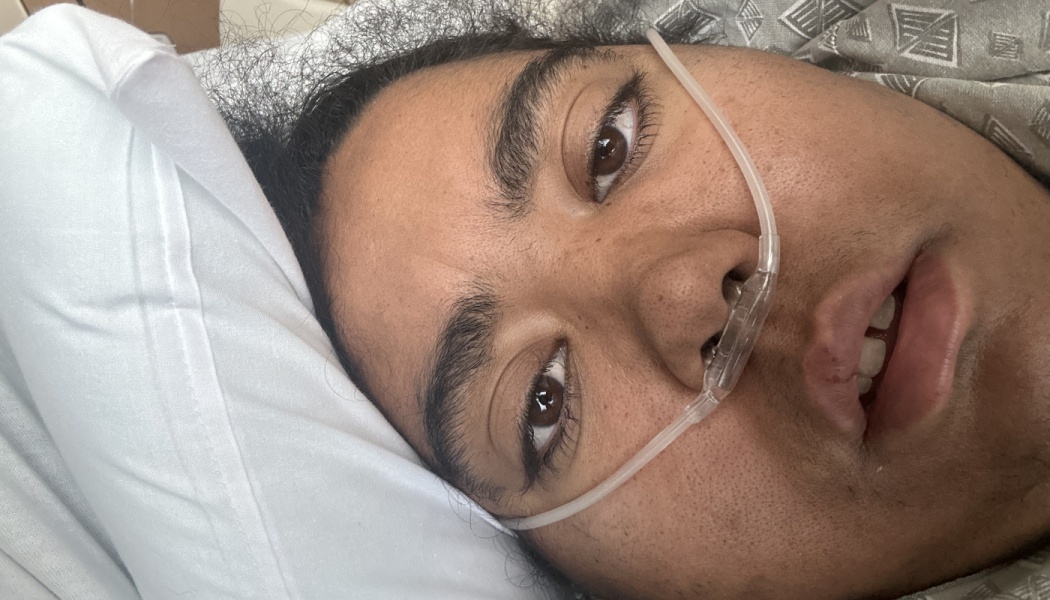 Close-up of a person lying in a hospital bed resting on a pillow while wearing a nasal cannula.