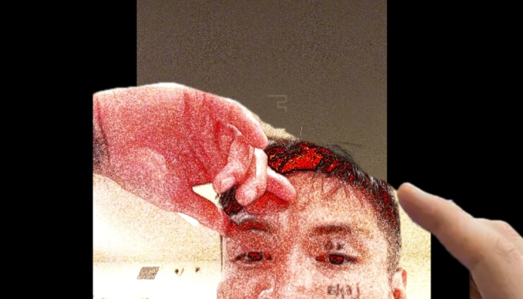 A finger touches a screen displaying a grainy, red-tinted close-up portrait of a young man.