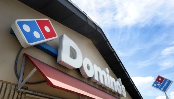 Domino's Pizza storefront sign and iconic red and blue logo against a blue sky.