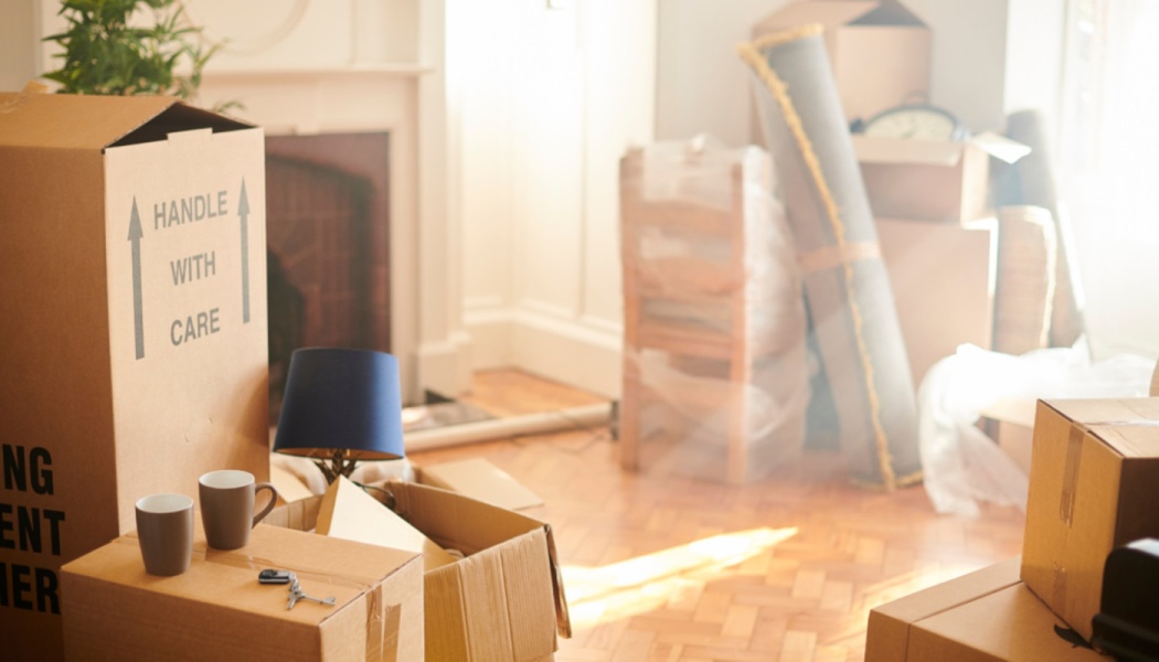 Cardboard moving boxes, coffee mugs, and house keys in a bright living room filled with packed belongings.