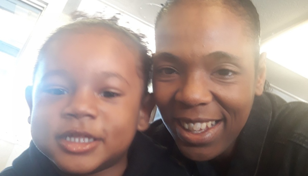 A smiling Black woman and young child pose closely together in a selfie.