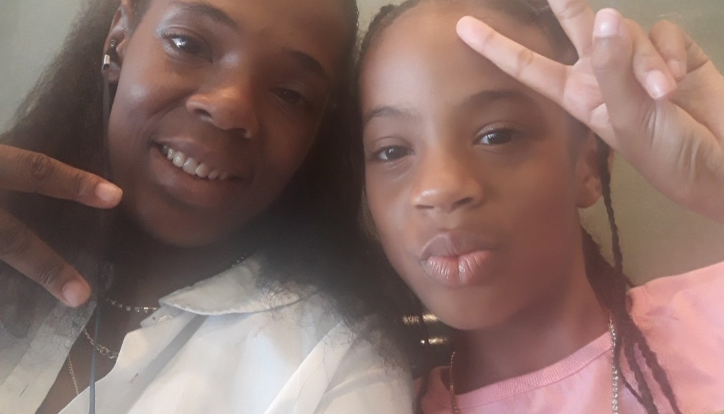A smiling woman and a young girl holding up peace signs during a close-up selfie.