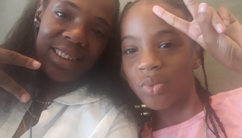 A smiling woman and a young girl holding up peace signs during a close-up selfie.