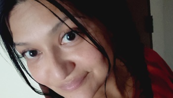 Close-up portrait of a woman with dark hair and dark eyes smiling softly at the camera.