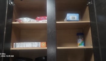 Open kitchen cabinet with mostly empty shelves containing a few scattered food items.