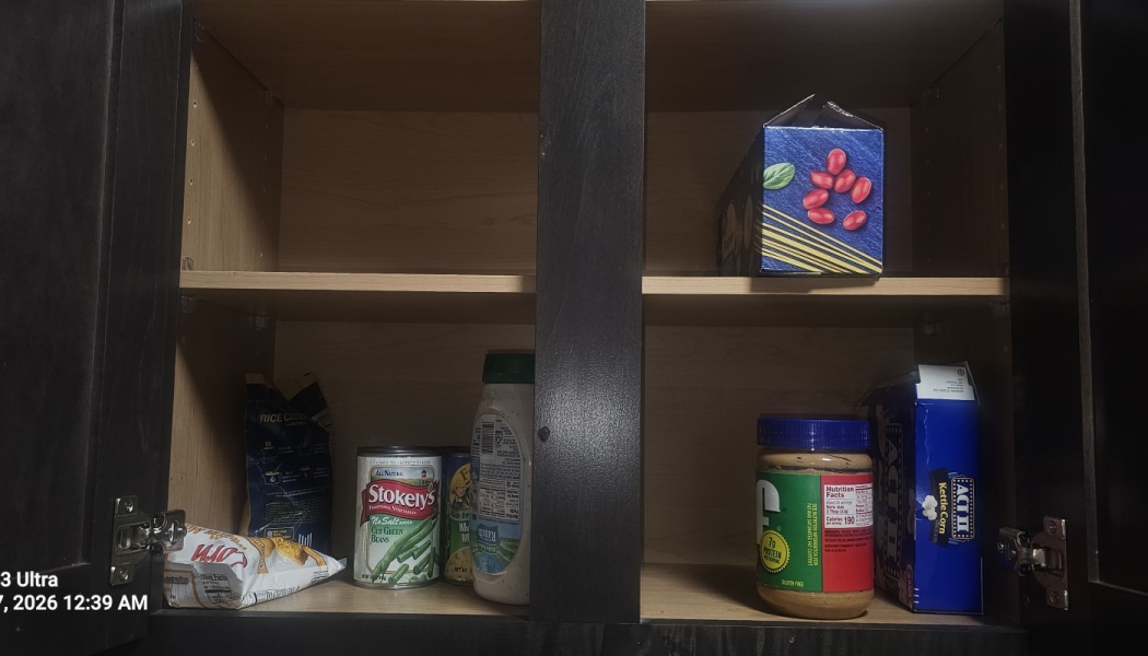 Mostly empty kitchen cabinet holding just a few canned goods, a box of pasta, and a jar of peanut butter.
