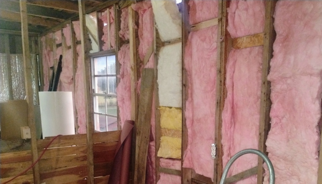 Pink fiberglass insulation installed between exposed wooden wall studs inside a room under renovation.
