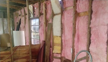 Pink fiberglass insulation installed between exposed wooden wall studs inside a room under renovation.
