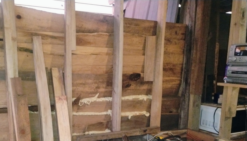Wooden wall framing under construction with spray foam sealant applied between horizontal planks.