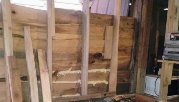 Wooden wall framing under construction with spray foam sealant applied between horizontal planks.