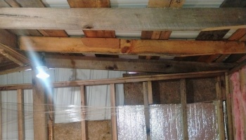 Exposed wooden roof rafters and wall framing in an unfinished building, illuminated by a hanging light bulb.