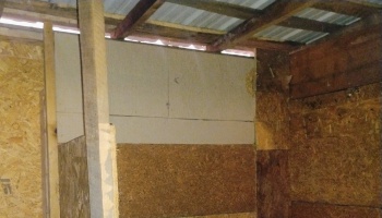 Rough, unfinished interior of a building with OSB and plywood walls under exposed wooden roof rafters.