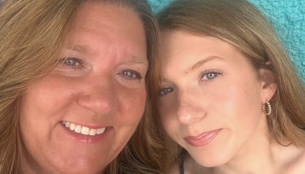 Close-up selfie of two smiling blonde women posing heads together against a bright turquoise background.