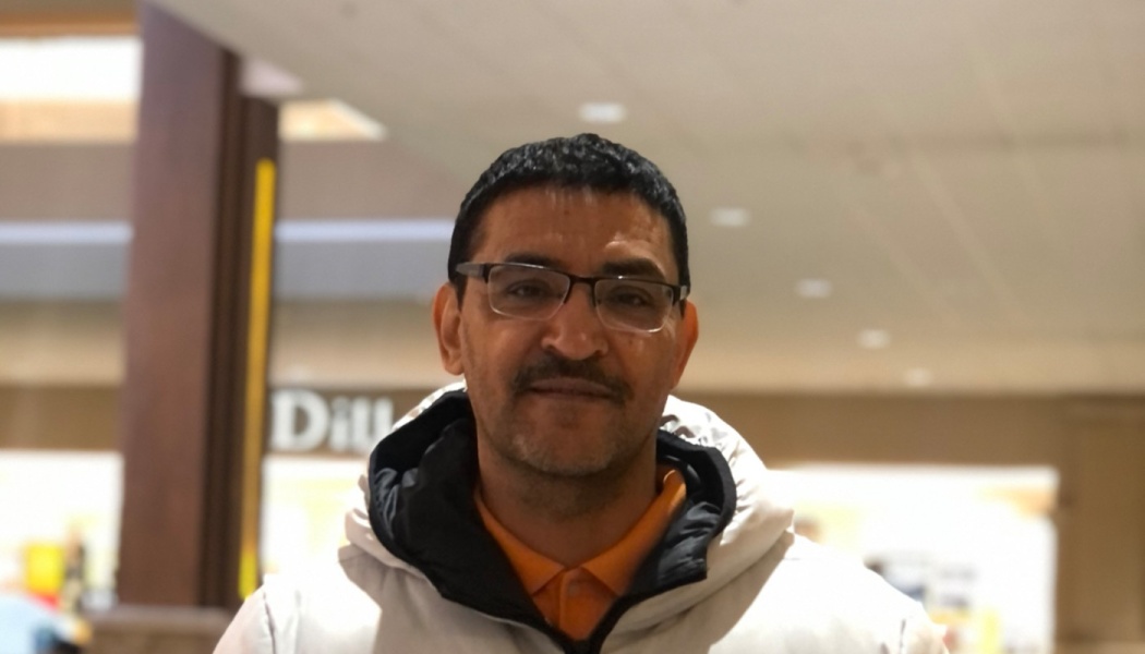 A middle-aged man with glasses and a mustache wearing a white hooded jacket and smiling at the camera.