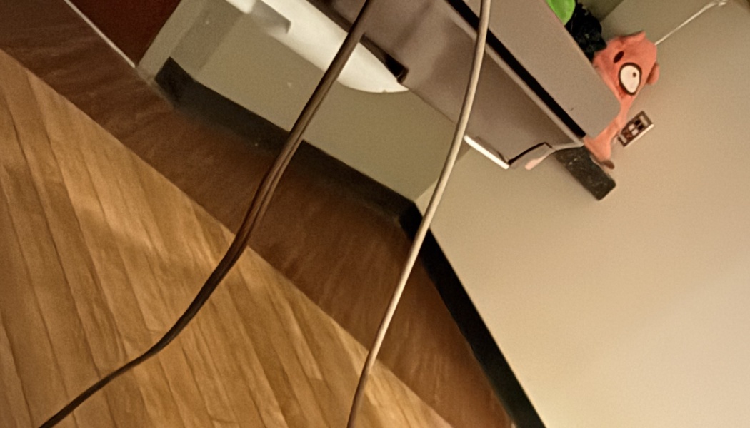Two cords hanging down toward wood flooring, with a pink plush toy sitting on a counter in the background.