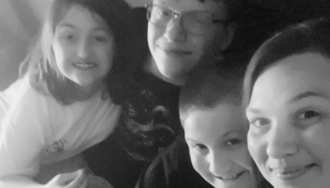 A smiling woman and three children gathered closely together in a black-and-white selfie.
