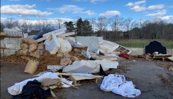 A large pile of discarded mattresses, sandbags, and trash dumped outdoors.