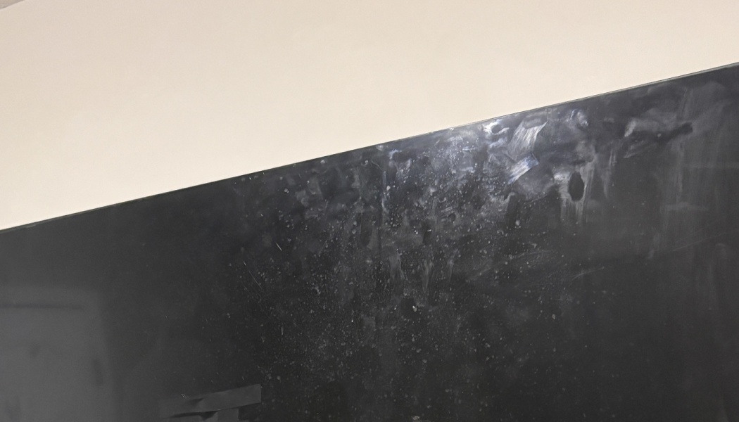 Dirty black screen covered in smudges, fingerprints, and dust spots against a light wall.