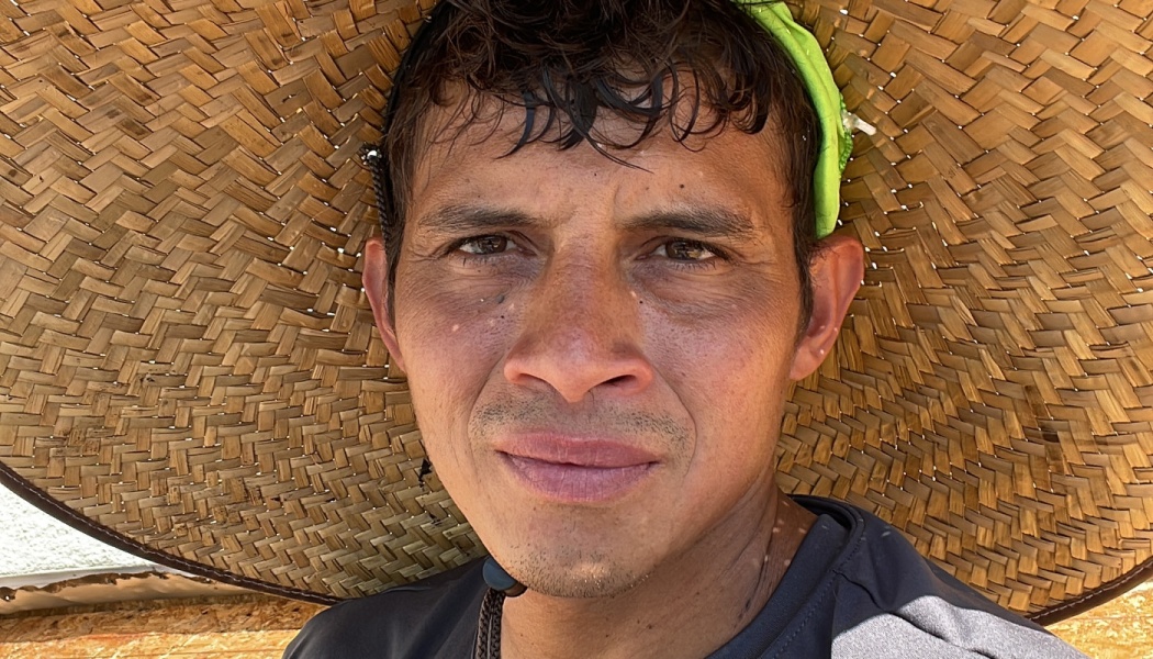 Close-up portrait of a man wearing a wide-brimmed woven straw hat looking directly at the camera.