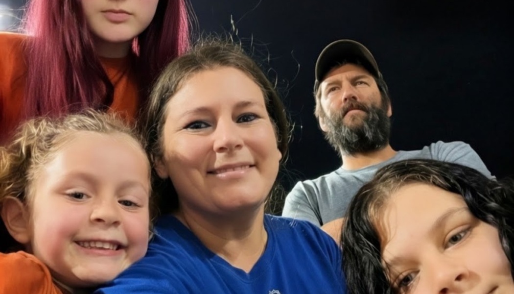 Family of five taking a close selfie together, with a smiling mother, bearded father, and three children.