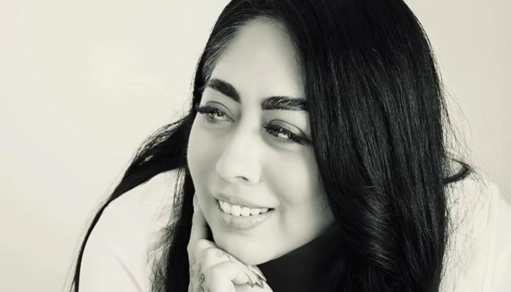 Black and white portrait of a smiling woman with long dark hair resting her chin on her hand.