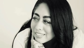 Black and white portrait of a smiling woman with long dark hair resting her chin on her hand.