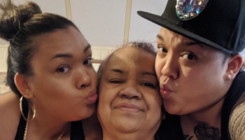 An older woman smiles in the center while two family members lean in on either side making kissy faces.
