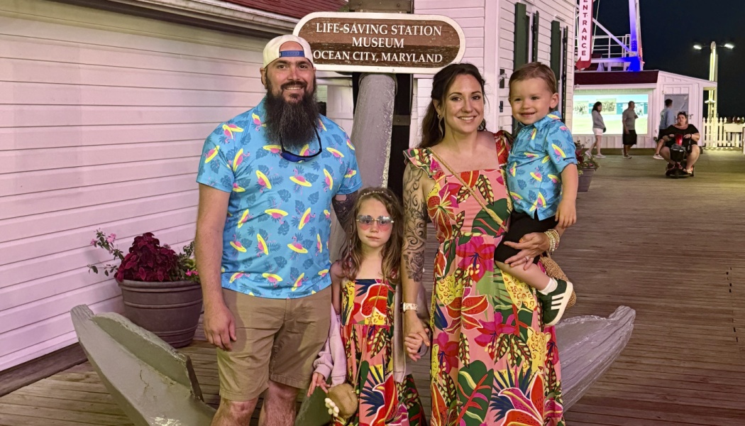 A family of four wearing colorful tropical clothing poses outside the Ocean City Life-Saving Station Museum.