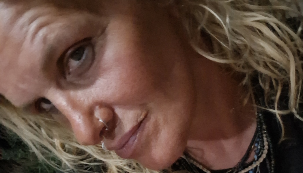 Close-up of a woman with blonde curly hair, a nose ring, and layered necklaces.