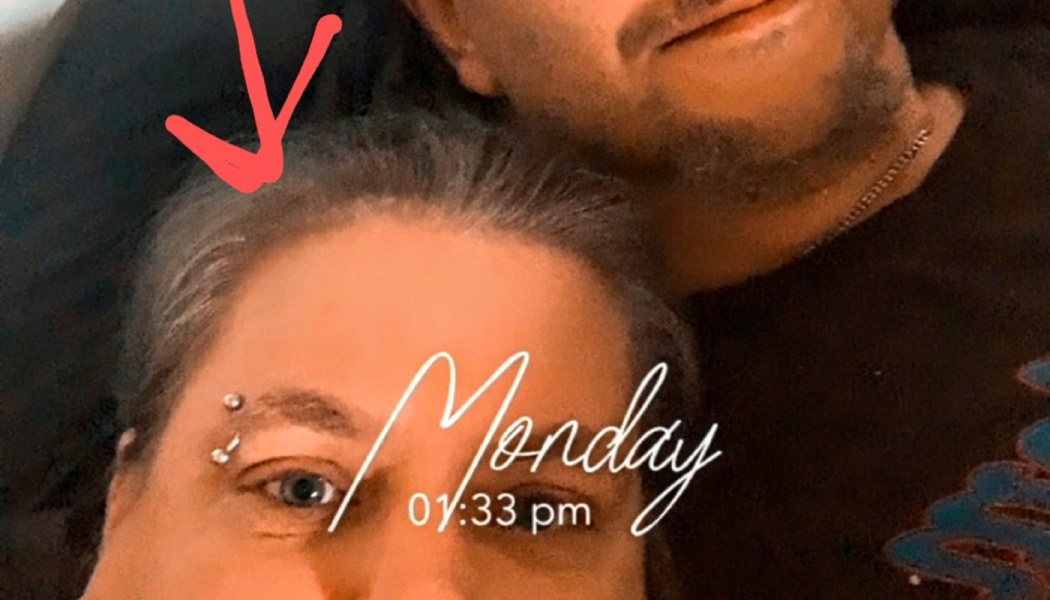 Close-up selfie of a person with an eyebrow piercing next to a man, with a red arrow pointing to their hair.