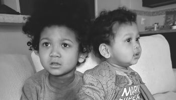 Two young children with curly hair sitting together on a sofa in a black-and-white portrait.
