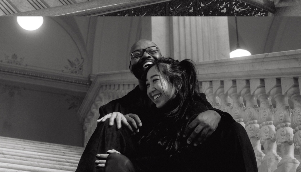 A smiling couple embracing joyfully while sitting on a grand marble staircase, in black and white.