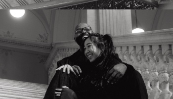 A smiling couple embracing joyfully while sitting on a grand marble staircase, in black and white.