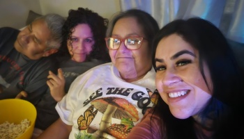 Four smiling family members relaxing together on a couch with a bowl of popcorn during a cozy movie night.