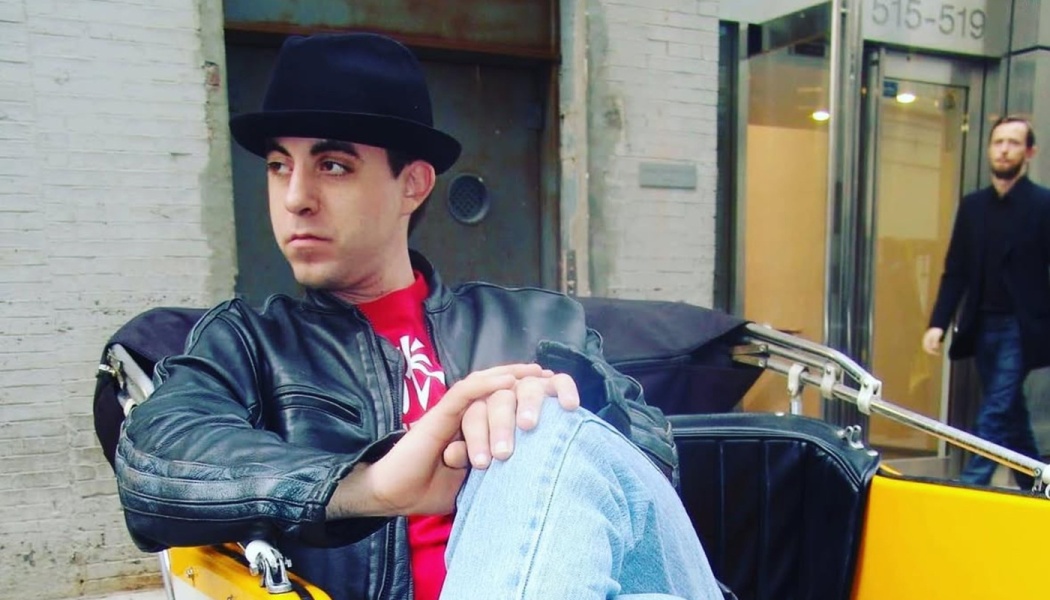 A man in a black hat and leather jacket sitting thoughtfully in a yellow rickshaw on a city street.