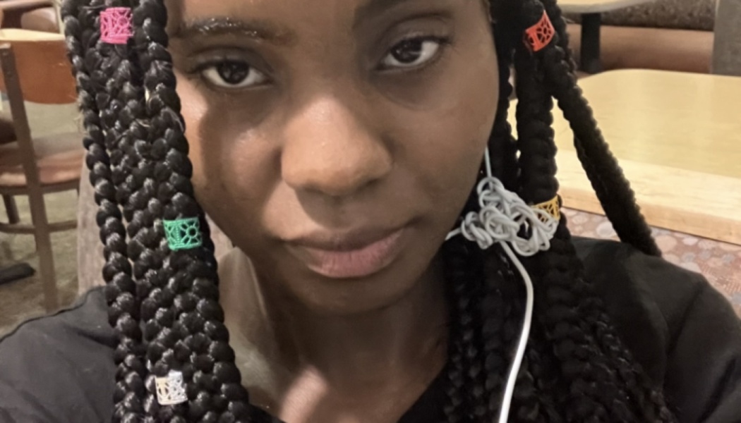 Close-up of a young Black woman with colorful cuffs on her long box braids looking at the camera.