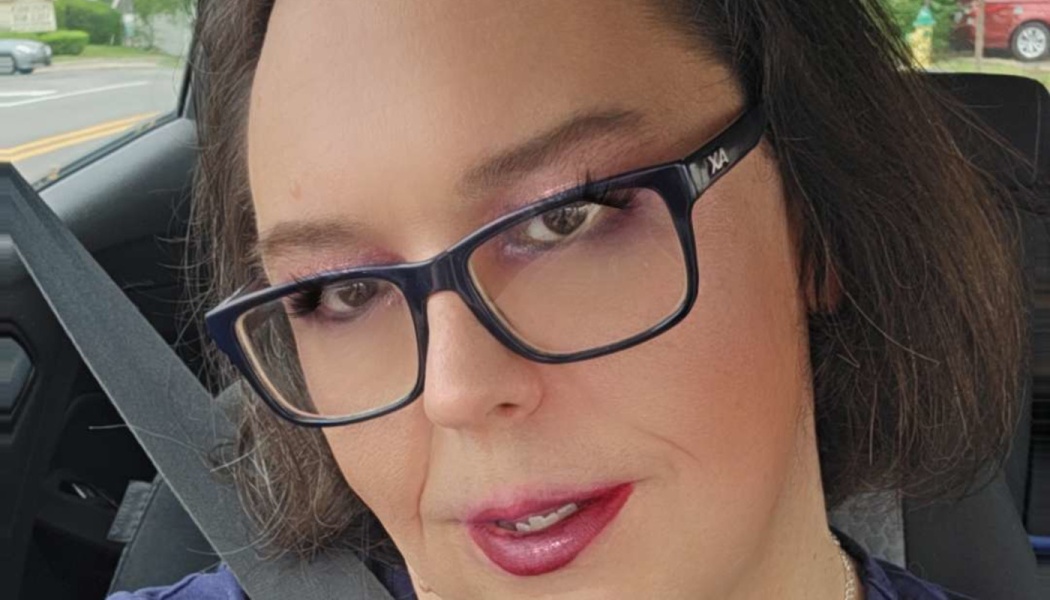 Close-up selfie of a woman with short dark hair, dark-framed glasses, and red lipstick sitting in a car.