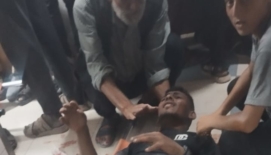 An injured young man lies on the floor in pain while an older man comforts him, surrounded by bystanders.