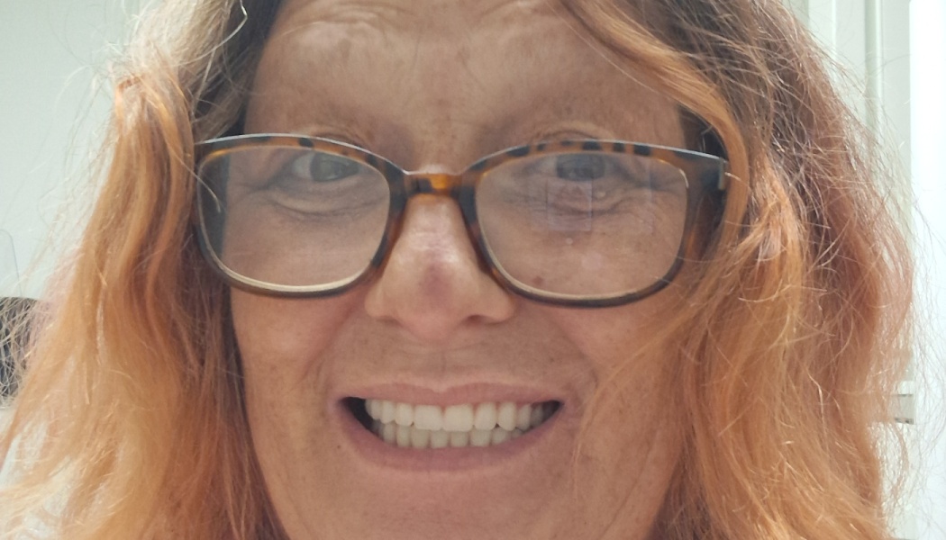 Close-up of a smiling woman with wavy reddish hair and tortoiseshell glasses.