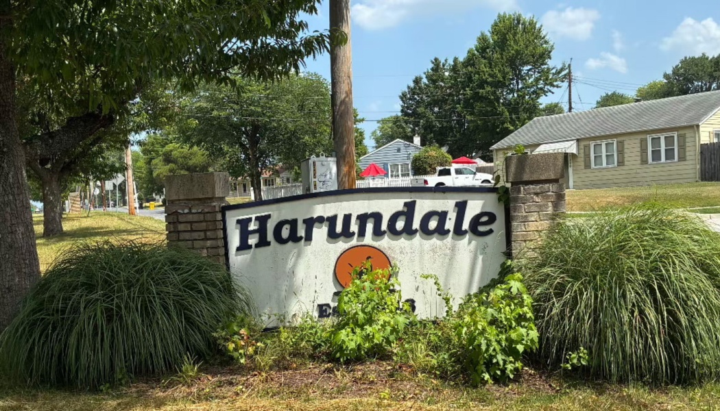 A neighborhood sign reading "Harundale" flanked by brick pillars and green bushes in a suburban area.