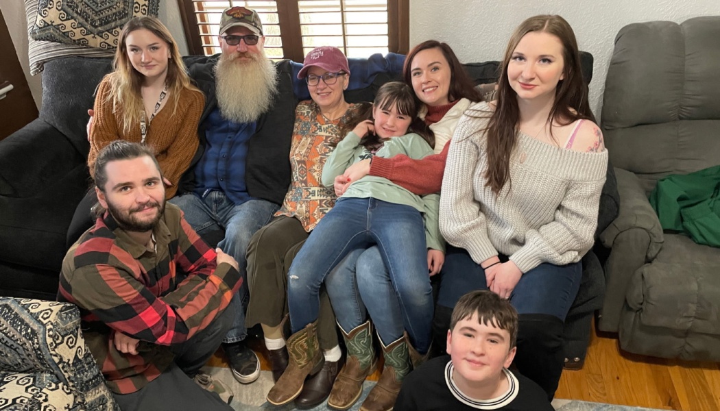 A multi-generational family of eight smiling together on a living room couch.