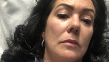 Close-up of a dark-haired woman lying down with a tired, somber expression.